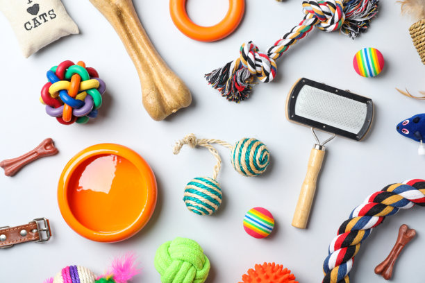一张俯视拍摄的平面照片，展示了各种色彩鲜艳的猫狗玩具、美容工具和配饰，散落在浅蓝色的背景上。图片下载