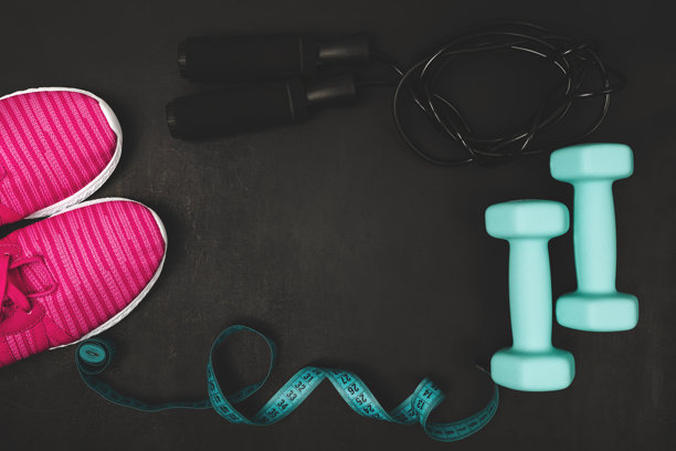 俯视粉色运动鞋、蓝色哑铃、跳绳和卷尺在深色背景上的照片，并留有复制空间，健身器材平面图概念图片下载