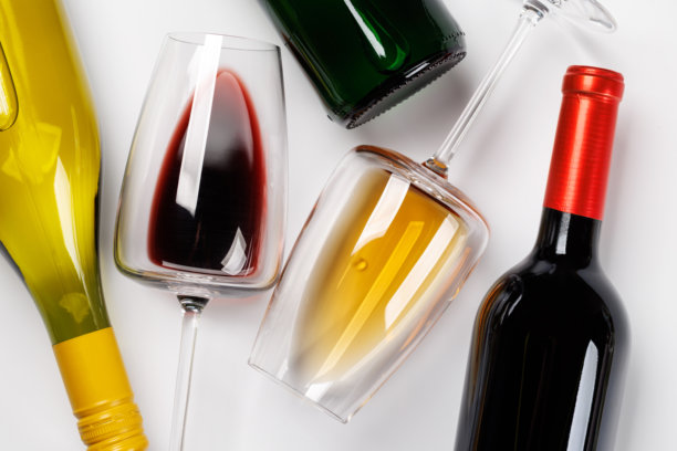 酒杯中盛有红酒和白酒，酒瓶横置于白色背景上图片下载