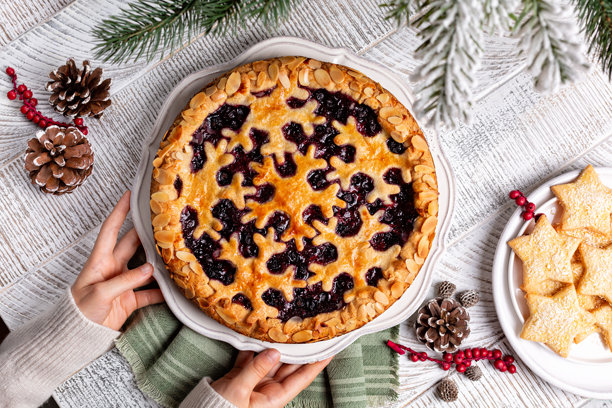 冬季圣诞或新年节日烘焙。手捧烤制的混合浆果杏仁酥皮派或挞，饰有雪花图案。木质白桌上摆放着自制星形饼干，俯视角度。图片下载