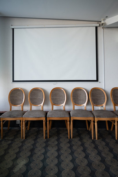 墙上挂着空白的投影幕布，幕布下方摆放着一排风格化的椅子——用于照片模拟图片下载