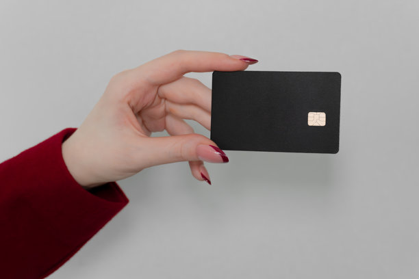 一张近距离拍摄的女性手部照片，展示了一张带有金色芯片的空白黑色信用卡，背景为中性灰色。图片下载