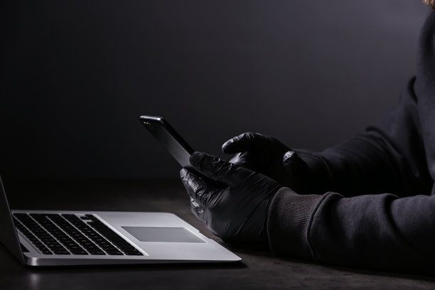 戴着手套的双手在完全黑暗中操作手机和笔记本电脑的特写照片，象征着高级别网络犯罪和非法活动。图片下载
