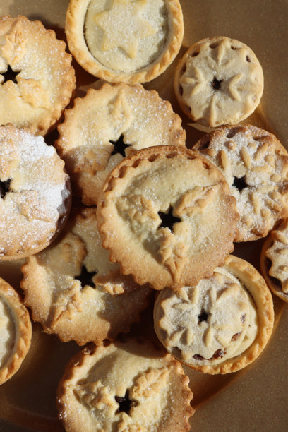 盛满圣诞馅饼的金色餐盘的完整画面，馅饼上堆叠着糕点星星、雪花或冬青叶造型的盖子，这是带有甜馅的节日圣诞酥皮点心，撒有糖粉，俯视角度。图片下载