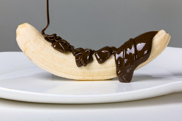 一块融化的巧克力均匀地覆盖着一根香蕉，巧克力顺着香蕉滴落到干净的白盘上。该系列共有9张照片。图片下载