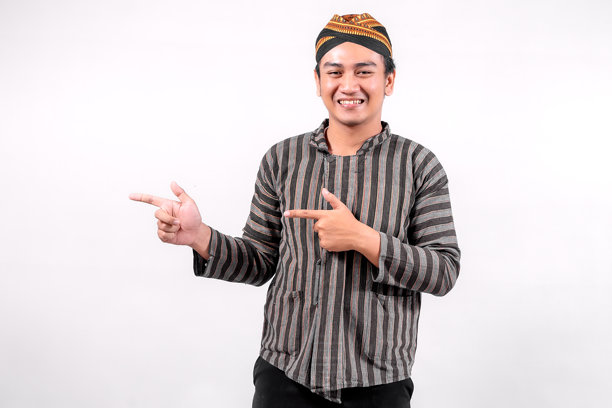 这张照片展示了一位身着传统鲁里克服饰的年轻男子，他面带微笑，用手势表达，在简洁的背景下展现出文化自豪感和友善。图片下载