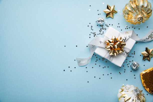 一张优雅的节日俯拍照片，以金色主题的礼品盒、闪亮的装饰品和星星为特色，在时尚的浅蓝色背景上营造出节日的氛围。图片下载