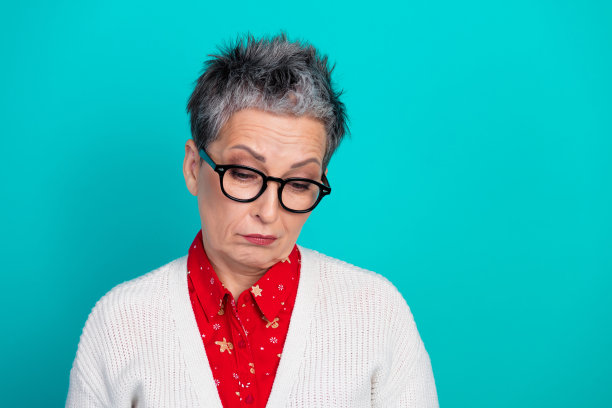 一位优雅的老年女性，身穿红色圣诞衬衫和白色开衫，在蓝绿色的背景前温柔地微笑，适合节日季的素材图片下载