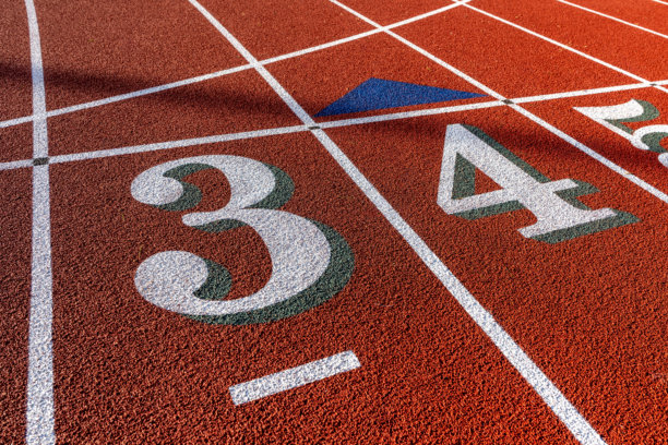 特写照片，户外跑道的白色数字三、四，3、4，在新的红色跑道上带有绿色阴影和白色跑道线。图片下载