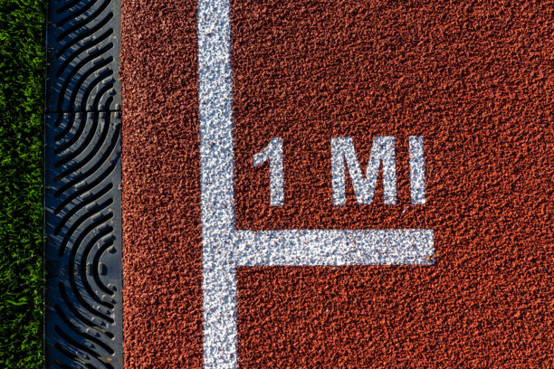 全新红色跑道上的英里（1 mile, 1 MI）标志特写照片，跑道有白色线条。图片下载