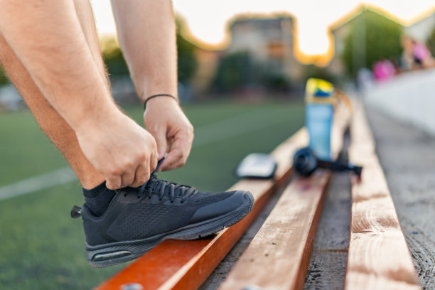一名超重男子在运动跑道上跑步前系鞋带的特写照片。图片下载