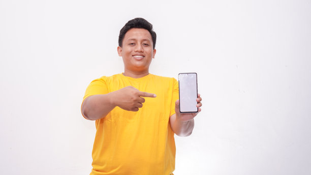 一个亚洲胖男人手里拿着智能手机，对着镜头展示白色屏幕，并用手指指向你。图片下载