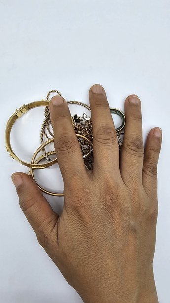 戴着手镯和戒指的女性手部特写，手部覆盖着黄金。黄金作为一种长期投资工具，尤其受女性青睐，购买黄金首饰进行投资。图片背景为白色。图片下载