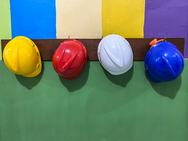 色彩鲜艳的安全帽，黄色、红色、白色和蓝色，整齐地挂在医院工作区域附近的一排。这张图片代表了医疗环境中的安全、维护和团队合作。图片下载