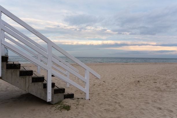 宁静的现代白色木质栏杆和混凝土楼梯照片，在美丽柔和的暮光或日落时分，向下延伸至宽阔金色的沙滩。图片下载