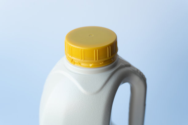 从高处拍摄的宏观照片，精确聚焦于牢固固定白色塑料液体容器的亮黄色带肋螺纹盖。图片下载