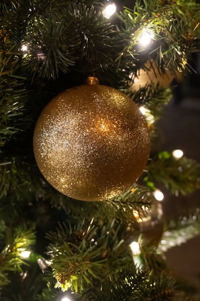 一张垂直的特写照片，捕捉了一个大的金色闪光圣诞挂饰的耀眼光线反射和精细的颗粒纹理。图片下载