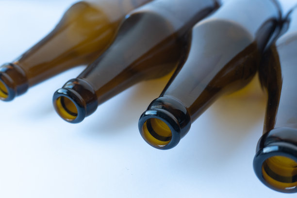 俯拍的横幅照片，展示了四只空棕色啤酒瓶平放在干净的白色表面上的瓶颈和瓶口。图片下载