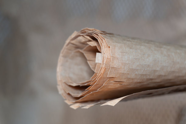 特写照片，展示一段卷起的棕色蜂窝状保护包装纸，突出其纹理分层的材质，聚焦于可持续性和环保物流。图片下载