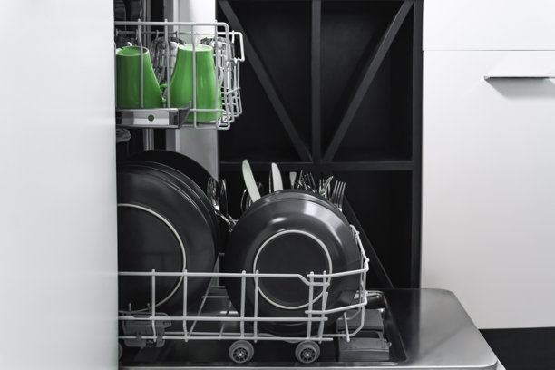 一张敞开的现代洗碗机的照片，展示了装满黑色碗碟的底层架，以及准备清洗的顶层架上的绿色马克杯。图片下载