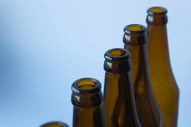 特写照片，四只空棕色啤酒玻璃瓶的瓶颈，呈阶梯状向上倾斜排列，背景为明亮柔和的蓝色。图片下载