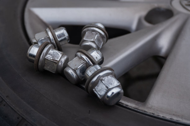 特写照片，展示了在更换轮胎时，五个闪亮的银色金属轮毂螺母放置在汽车轮胎和合金轮辋上的场景。图片下载