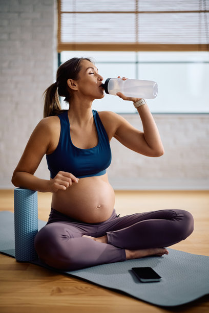 一位年轻的孕妇在家锻炼时喝水。图片下载