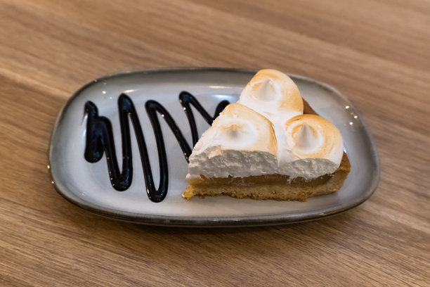 特写照片，捕捉到一块美味的柠檬酥皮派，上面用深色巧克力酱装饰，放在一个风格化的灰色盘子上。图片下载