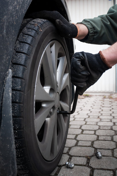 技师或驾驶员在常规换胎服务中，使用扳手拧松汽车合金轮毂上的螺母的照片。图片下载