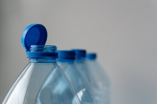 特写照片，画面前景为透明塑料瓶敞开的蓝色瓶盖和瓶颈，另外两瓶瓶身在柔和的背景中逐渐模糊，暗示着易于取用和使用。图片下载