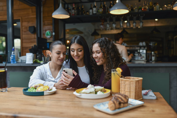 三位朋友在休息酒吧享用早餐，同时在手机上分享照片图片下载