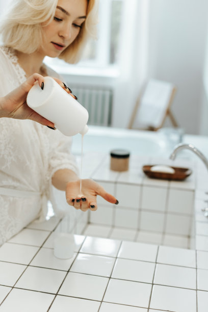 女性在浴室中从瓶子里倒出洗发水图片下载