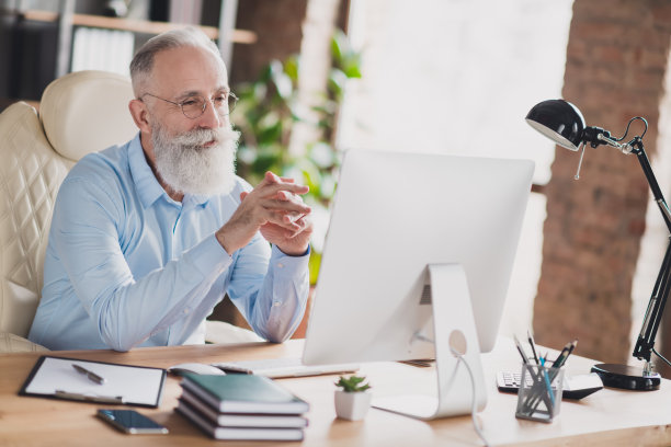 照片：一位快乐微笑、留着胡子的工人，戴着眼镜，穿着蓝色衬衫，在工作室的工位上使用现代设备工作图片下载