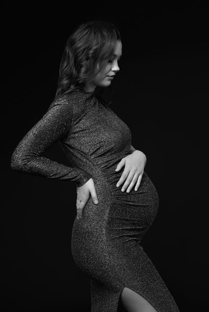 身着亮片连衣裙的孕妇的黑白肖像，双手放在孕肚附近。图片下载