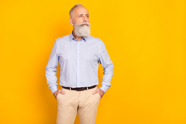 照片：一位梦想着、年迈而迷人的男士，双手插在口袋里，目光空洞地望向远方，背景是闪耀的黄色。图片下载