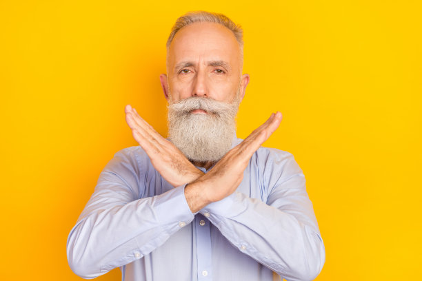 照片：蓄着胡须的严肃中年男子身穿蓝色衬衫，双臂交叉，背景为黄色图片下载