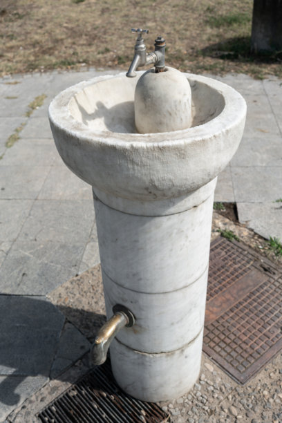 带有金属水龙头的古老石制喷泉。这张照片展示了城市户外空间公共基础设施和供水概念。竖构图图片下载