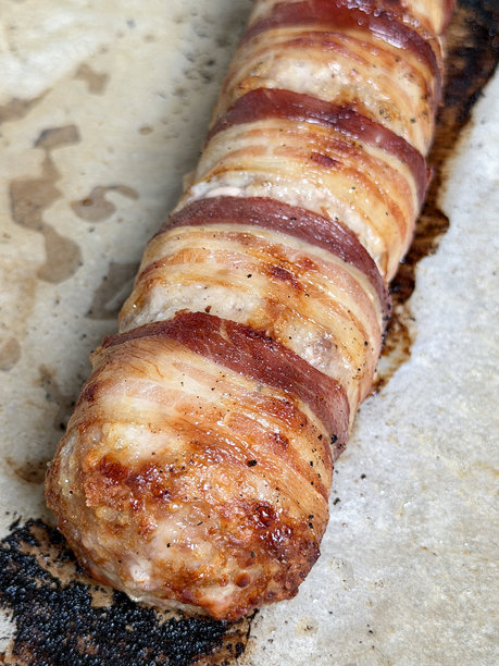 全画幅圣诞晚餐食材图片，烤盘上铺着烘焙纸，上面放着巨大的香肠卷（培根包裹的猪肉香肠），俯视角度拍摄。图片下载