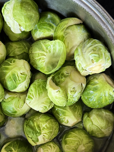 俯视拍摄的圣诞晚餐食材全画幅图片，金属锅里装着刚洗净、剥好皮的抱子甘蓝，表面有水珠和水滴，还有凝结的水汽。图片下载