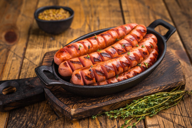 多汁烟熏煎香肠放在木板上，配有香草和叉子。高质量图片，适合餐厅菜单或美食博客标题。图片下载