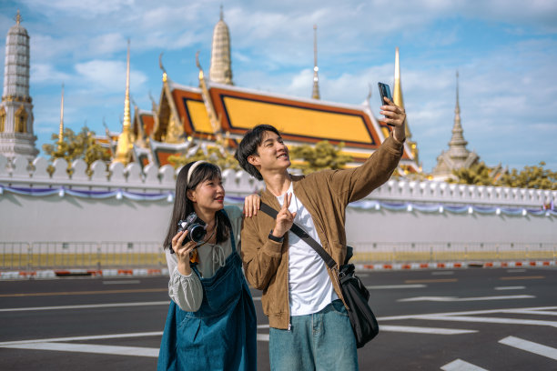 珍藏回忆：一对亚洲游客情侣在曼谷大皇宫前用手机开心自拍，记录下他们的旅程图片下载