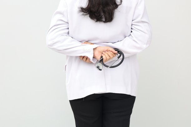 近距离照片，聚焦于一名身穿医生袍的站立医生，他将听诊器放在身后，背景为白色。图片下载