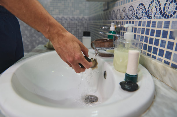 一个人在瓷砖浴室的水槽旁洗手，旁边有皂液器和水龙头，体现了清洁的概念图片下载