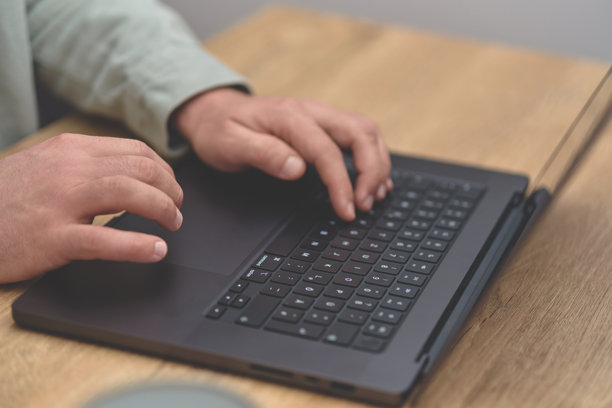 特写图片，展示商务人士在木质办公桌上操作笔记本电脑键盘的双手。图片下载