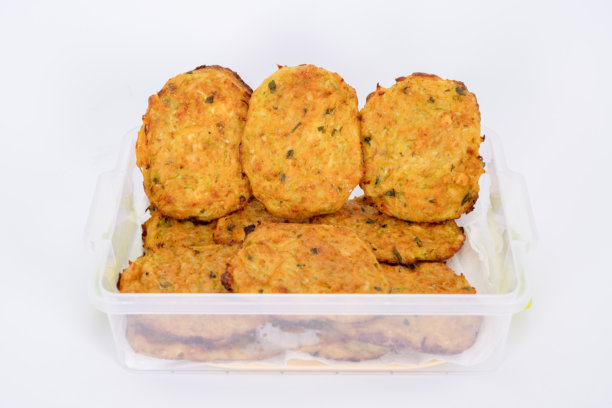 一张特写照片，展示了用塑料透明容器整齐摆放的自制蔬菜煎饼。这些金黄酥脆的煎饼外表看起来酥脆，可以看到里面有香草和蔬菜的碎末。图片下载