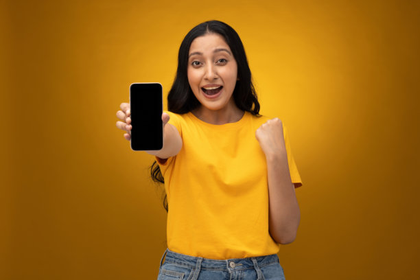 年轻女子展示手机屏幕，背景为黄色，孤立的图片图片下载