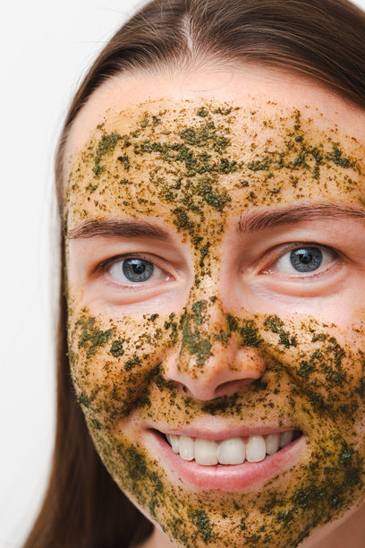 特写一名年轻女子，脸上敷着绿色天然自制面膜，背景为白色。居家或沙龙的自我护理概念。面部特写，竖幅照片图片下载