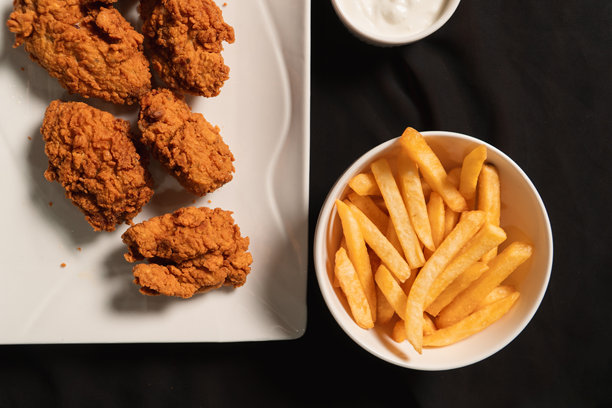 俯视视角拍摄的炸鸡和薯条放在黑色布上的照片。图片下载