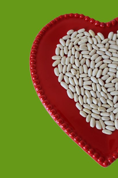 垂直照片，盘子是红色的，背景是青柠绿，上面放着干燥的生白芸豆种子。有谷物纹理。烹饪、蔬菜、健康饮食、准备的概念。图片下载