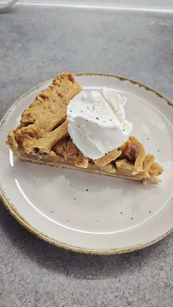 陶瓷盘中盛放着自制苹果派的切片，上面装饰着鲜奶油。该图片代表着温馨的甜点时光、家庭烘焙和经典的慰藉食品。图片下载